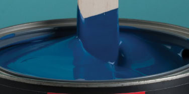 Stirring blue paint in an open can.